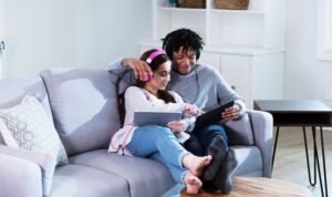 Young multiracial couple using digital tablets on sofa